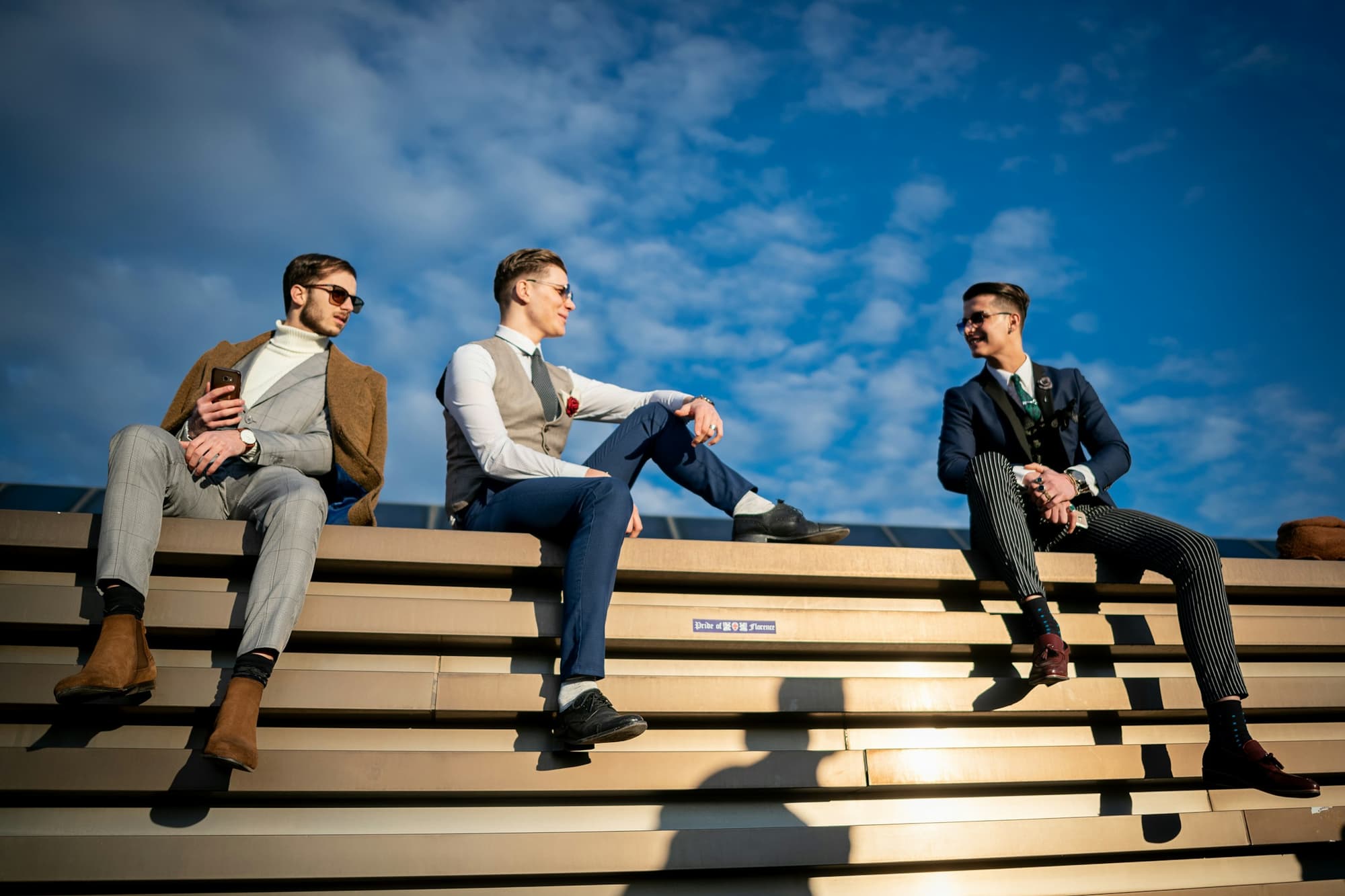 Three men in tailored suits sitting on wide concrete steps under a blue sky